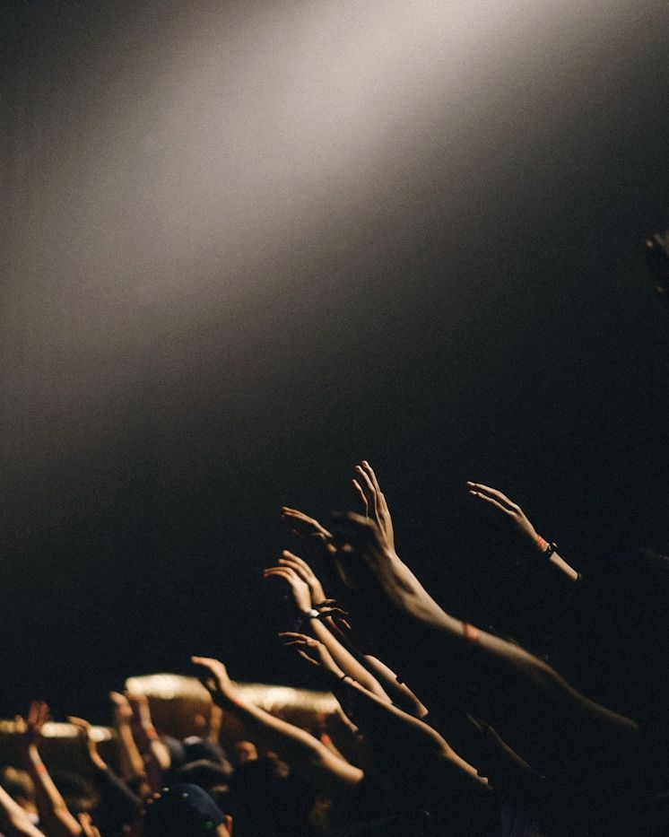 Hands reaching upward in warm concert light